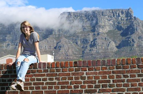 Brenna in Cape Town sitting on a brick wall with the iconic Table Mountain behind her.