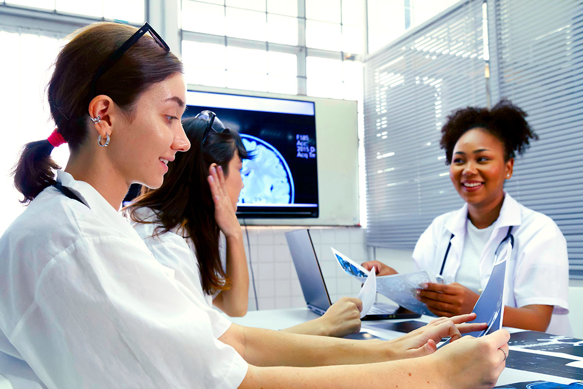 three young medical professionals sitting around a table talking and looking at X-Ray images