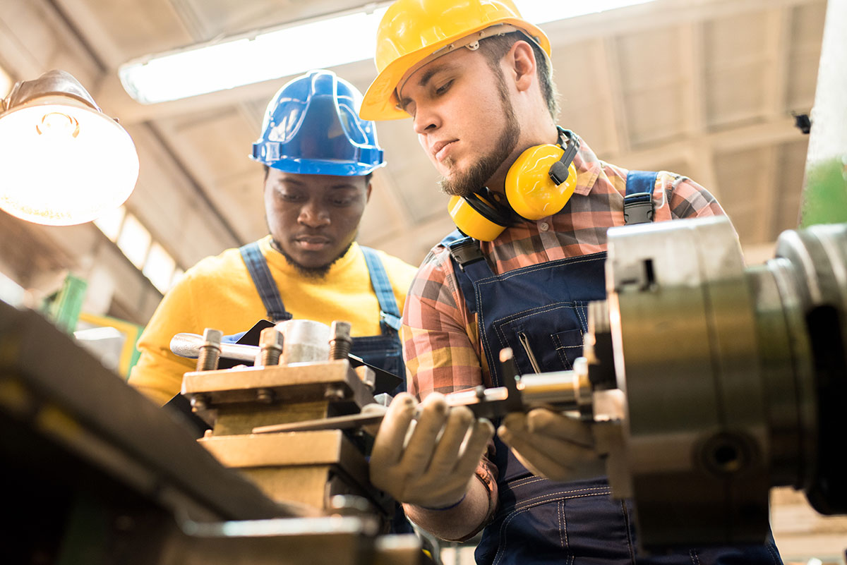 two machinists wearing hardhats and working 