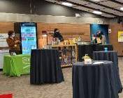Theater lobby with cocktail tables, display booths, and people standing near exhibits.